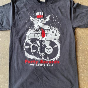 以下が含まれることがあります： 黒っぽいグレーのTシャツ。シルクハットをかぶり、赤い舌を出した漫画のオオカミが描かれています。オオカミは3枚のレコードの上に座っています。「Party Records for Adults Only」の文字が赤色でプリントされています。