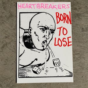 Puede incluir: Ilustración en blanco y negro sobre una tarjeta blanca. La imagen presenta una persona calva con la boca abierta, escupiendo dados. El texto dice "HEARTBREAKERS" en rosa y "BORN TO LOSE" en rojo.
