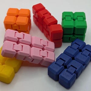May include: A collection of colorful fidget toys in orange, red, green, pink, yellow, and blue. Each toy is composed of connected, interlocking blocks. The toys are designed to be manipulated and provide tactile sensory input.