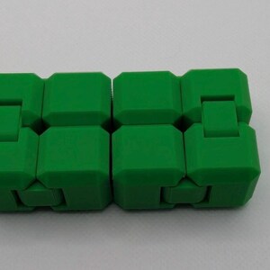 May include: A bright green fidget toy, composed of eight connected, cube-shaped blocks. Each block has a small, rectangular extension that allows the toy to bend and move. The toy is designed to be manipulated and played with.