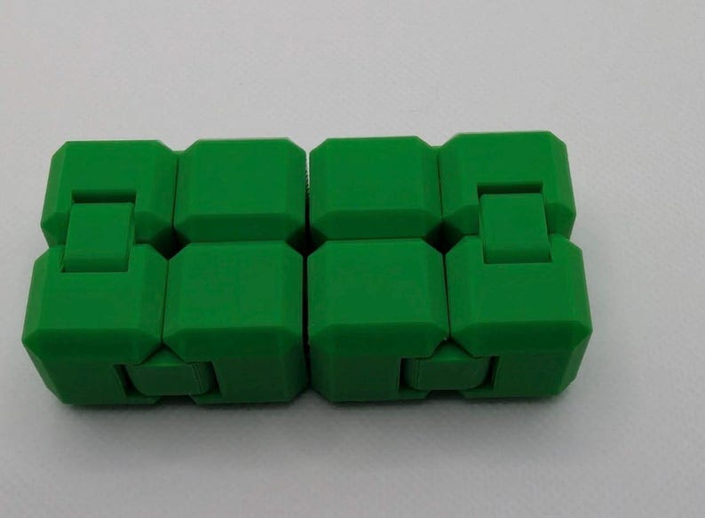 May include: A bright green fidget toy, composed of eight connected, cube-shaped blocks. Each block has a small, rectangular extension that allows the toy to bend and move. The toy is designed to be manipulated and played with.