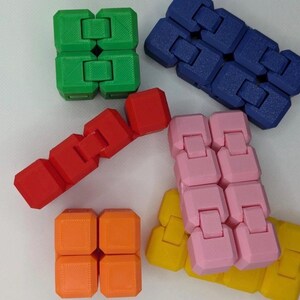 May include: An assortment of colorful fidget toys in green, blue, red, pink, orange, and yellow. The toys are made of connected blocks that can be manipulated. The image is taken from a high angle, with the toys arranged on a white surface.