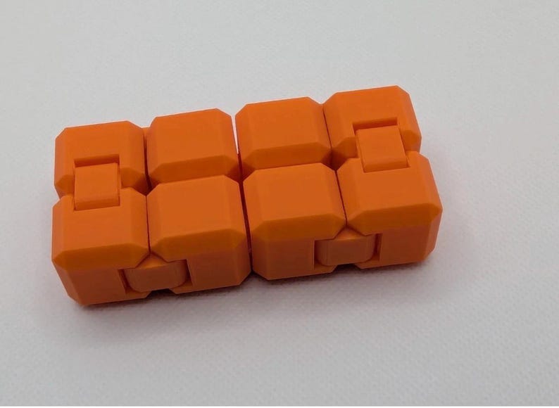 May include: An orange fidget toy, composed of interconnected, rectangular blocks. The blocks are a vibrant, solid orange color and are designed to move and flex. The toy is shown against a white background.