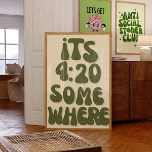 May include: A framed poster with a green background and white text that reads "ITS 4:20 SOMEWHERE". The poster is hanging on a wall in a room with wooden floors.
