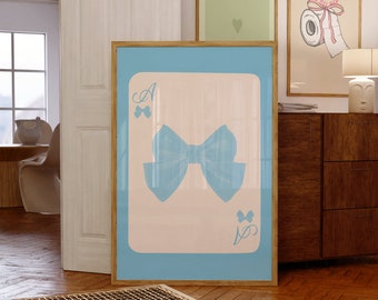 May include: A framed art print featuring a light blue bow on a playing card design. The print is set against a light pink background with a light blue border. Other framed prints are visible in the background.
