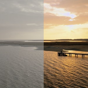 May include: A wooden pier extends out into a body of water with a person standing at the end. The water is calm and reflects the golden light of the setting sun. The sky is a soft orange and pink.
