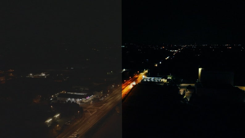 May include: A night time aerial view of a city with a highway running through the center. The highway is lit up with streetlights and car headlights. The city is mostly dark, but there are some lights from buildings and houses.