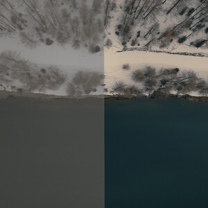 May include: An aerial view of a snowy forest with a path leading to a river. The river is a dark blue color and the forest is covered in white snow.