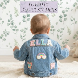 May include: A light blue denim jacket with the name "ELLA" embroidered on the back in pastel colours. The jacket features patches of a rainbow, a butterfly, and a bow. The background includes floral wallpaper and the text "LOVED BY 33K+ CUSTOMERS".