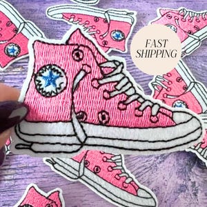 May include: Embroidered pink high-top sneaker patches with white laces and soles. Each patch features a blue star logo. The patches are scattered on a purple surface. The text "FAST SHIPPING" is on a circular sticker.