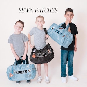 Puede incluir: Tres niños sosteniendo bolsas de lona personalizadas. Las bolsas son de color azul claro y negro, adornadas con parches y nombres como "Brooks", "Vinny" y "Jack". La imagen está etiquetada como "SEWN PATCHES".