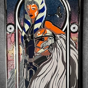May include: A rectangular metal pin featuring two characters from Star Wars. One character has orange skin and white and blue head tails. The other character is wearing an orange helmet. The background is blue and red.