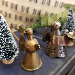 May include: Three small angel figurines, two are made of metal and one is made of brass. The metal angels are holding a small plate and a small tree. The brass angel is standing on a small base.