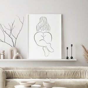 May include: A black and white line drawing of a person lying on their stomach with their legs bent. The drawing is on a white background and is framed in a white frame.