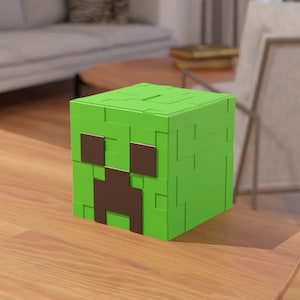 May include: A green cube-shaped object with a pixelated design, featuring a brown face. The object is on a wooden surface. The design is reminiscent of a character from a popular video game.