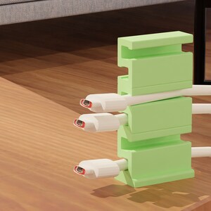 May include: A green cable organiser with three white cables running through it. The organiser is made of plastic and has a rectangular shape.