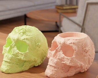 May include: Two decorative skull candle holders, one in a light green colour and the other in a light pink colour. Both skulls have intricate floral designs.