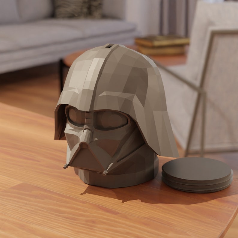 May include: A gray, geometrically-shaped Darth Vader head figurine with a black face mask. The figurine is sitting on a wooden surface next to a stack of gray coasters.
