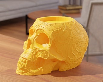 May include: A yellow ceramic skull with intricate paisley patterns. The skull has a hollow top, which could be used as a candle holder or a decorative planter.
