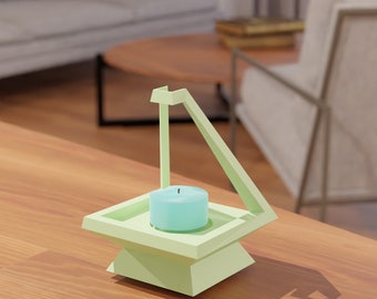 Puede incluir: Un portavelas geométrico verde claro con una vela turquesa. El portavelas tiene una base cuadrada y una estructura de soporte triangular. El portavelas está sobre una mesa de madera.