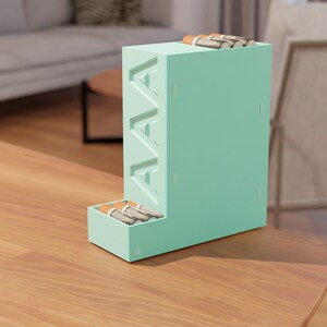 Puede incluir: Un organizador de baterías de color verde claro con las letras "AAA" impresas en el lateral. El organizador tiene un cajón para guardar las baterías y un compartimento para mantener las baterías en posición vertical.
