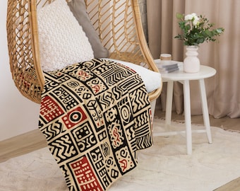 Può includere: Una coperta in tessuto intrecciato con un motivo geometrico in nero, rosso e crema. La coperta è drappeggiata su una sedia in vimini.