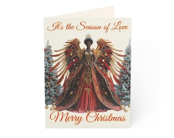 May include: A Christmas card featuring a Black angel with golden wings and a red gown, standing in front of two Christmas trees. The text "It's the Season of Love" is at the top of the card, and "Merry Christmas" is at the bottom.