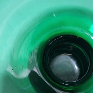 May include: A close-up view of the inside of a deep green glass vase. The vase has a wide opening and a narrow base, creating a funnel-like shape. The glass is smooth and reflective, showing a slight swirl pattern.