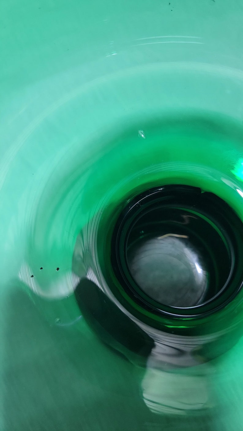May include: A close-up view of the inside of a deep green glass vase. The vase has a wide opening and a narrow base, creating a funnel-like shape. The glass is smooth and reflective, showing a slight swirl pattern.
