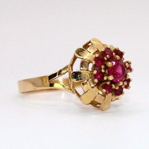 Puede incluir: Un anillo de oro con un grupo de piedras de rubí rojas engastadas en un diseño tejido.