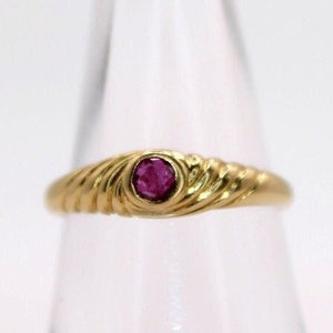 Könnte beinhalten: Ein goldener Ring mit einem gedrehten Band und einem einzigen roten Edelstein in der Mitte.