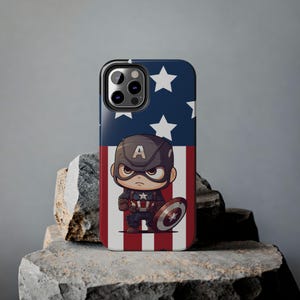Könnte beinhalten: Eine Handyhülle mit einem Cartoon-Bild von Captain America vor einer amerikanischen Flagge. Die Hülle ist schwarz mit einem durchsichtigen Rücken und einer erhöhten Kamerabuckel.