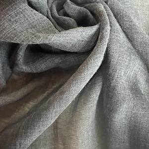 May include: A close-up shot of a gray scarf with a woven texture. The fabric is draped and swirled, creating a soft, flowing appearance. The scarf's color is a muted gray, and the weave is visible throughout the material.
