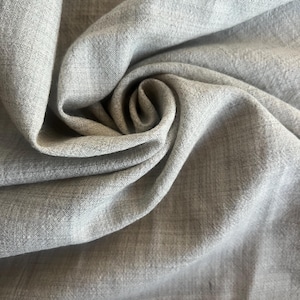 May include: Close-up of a light gray linen fabric with a subtle woven texture. The fabric is draped and folded, creating soft shadows and highlights. The material appears to be lightweight and breathable, suitable for clothing or home decor.