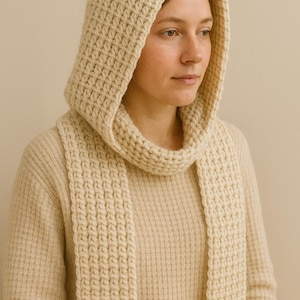 May include: Cream-colored knitted hood and scarf set. The hood is designed with a textured, chunky knit, and the scarf hangs down the front. The set is made of a soft, warm material, perfect for cold weather. The outfit is a neutral color.