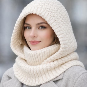 May include: Cream-colored knitted hood and scarf set. The hood features a textured stitch pattern and frames the face. The scarf is a ribbed knit design. The set is made of a soft, warm material, perfect for cold weather.