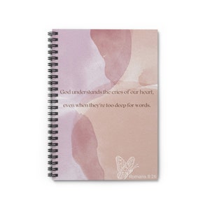 May include: A spiral bound notebook with a watercolor background in shades of pink and peach. The notebook features a white butterfly and the text "God understands the cries of our heart, even when they're too deep for words. Romans 8:26".