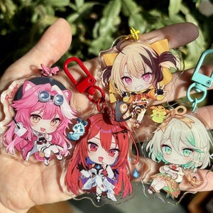 May include: Four anime character keychains with clear acrylic backgrounds. The characters are all female and have different colored hair and outfits. The keychains are attached to metal rings.