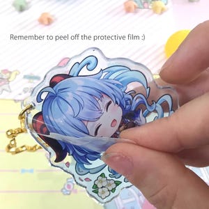 May include: A clear acrylic keychain with a colorful anime character illustration. The keychain features a blue-haired character with a pink bow and a white flower design. The protective film is still on the keychain. Remember to peel off the protective film.
