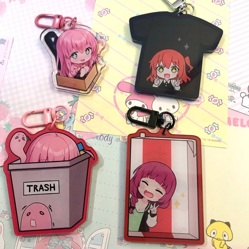 May include: Four different anime character keychains. Each keychain features a different character with pink hair and a different background. The keychains are made of clear acrylic and have a metal ring for attaching to keys or bags.