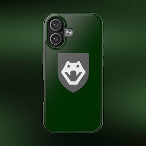 May include: A dark forest green smartphone case featuring a centered grey shield emblem with a white stylized wolf head graphic. The case has a dual-lens camera cutout at the top left corner with a circular flash element positioned to the right.