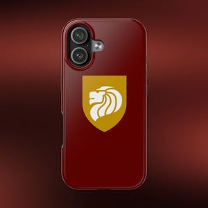 May include: A deep maroon smartphone case featuring a centered gold shield emblem with a white lion head profile. The case has a dual-lens camera cutout at the top left, with a glossy finish and rounded corners, providing a sleek protective cover.