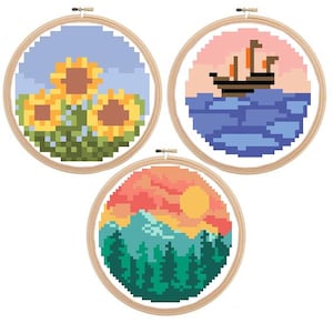 May include: Three embroidery hoops with different pixel art designs. The first hoop features a blue sky with three yellow sunflowers. The second hoop shows a blue ocean with a sailboat. The third hoop has a sunset over a mountain range with green trees.