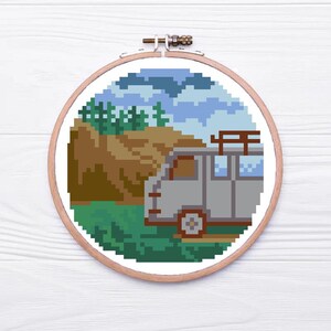 May include: A cross-stitch pattern of a gray van with a roof rack parked in front of a brown hill with green trees and a blue sky with white clouds.