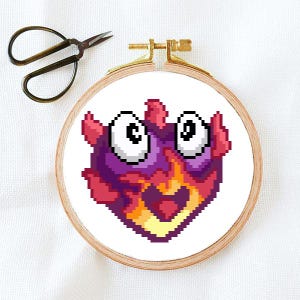 May include: Cross stitch pattern of a red, orange, and purple cartoon monster with big eyes and a wide open mouth. The monster is stitched on white fabric.