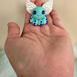 Pu&ograve; includere: Piccola statuina di polpo turchese con ali bianche glitterate e pois blu. La statuina ha grandi occhi espressivi e un viso sorridente. Il polpo &egrave; un artigianato stravagante e fatto a mano.