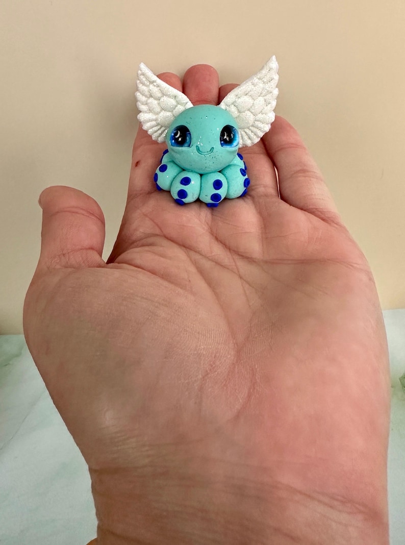 Pu&ograve; includere: Piccola statuina di polpo turchese con ali bianche glitterate e pois blu. La statuina ha grandi occhi espressivi e un viso sorridente. Il polpo &egrave; un artigianato stravagante e fatto a mano.