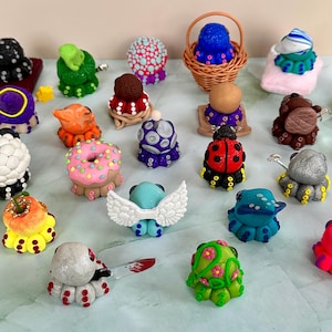 Pu&ograve; includere: Una collezione di figurine di polpo fatte a mano, in vari colori e design. La collezione comprende una coccinella, una ciambella e una creatura con le ali. Alcune sono in un piccolo cestino di vimini. Ogni statuina &egrave; unica.