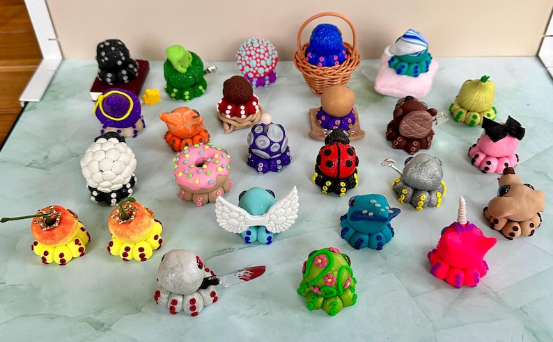 Pu&ograve; includere: Una collezione di figurine di polpo fatte a mano, in vari colori e design. La collezione comprende una coccinella, una ciambella e una creatura con le ali. Alcune sono in un piccolo cestino di vimini. Ogni statuina &egrave; unica.