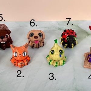 Pu&ograve; includere: Una collezione di otto figurine di argilla fatte a mano. Le figure includono un polpo, un gatto, una cipolla, un cane, un castoro, una coccinella e un polpo con un coltello. Ogni figura &egrave; dai colori vivaci e dettagliata, che mostra un design unico.